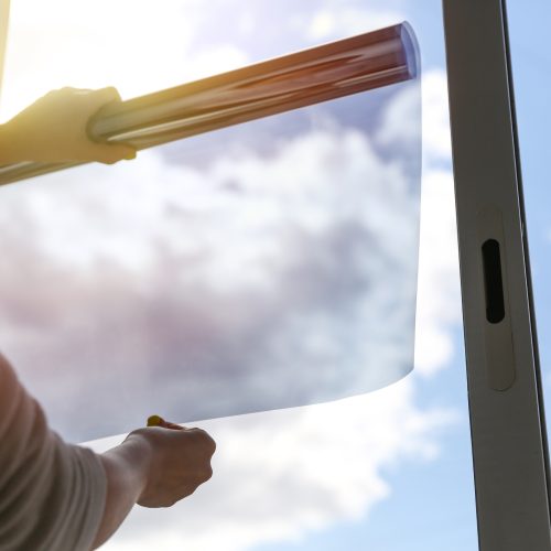 tinted glass in the house. window dimming by dark film. hands apply tint film to the window. tint film on sky background. sky view through tinted glass